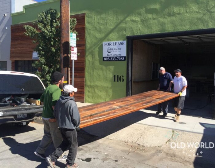 A crew of four men carrying a big reclaimed wooden plank