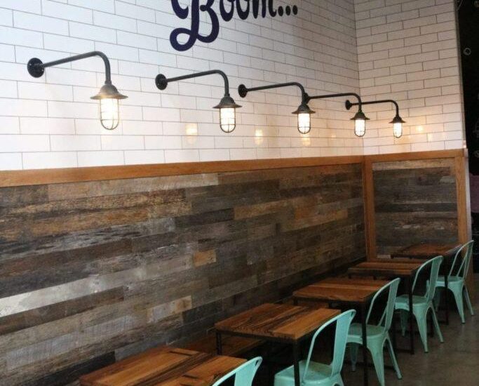 Five light blue chairs in front of five wooden tables under five lamps at the Crank & Boom ice cream shop In Manchester