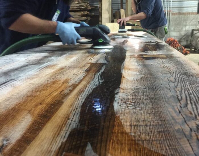 Two workers polishing a reclaimed wooden table with wood polishing tools