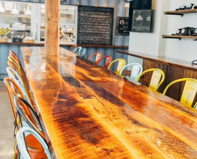 17 multicolored chairs around a reclaimed wood bar table In the Lama Dog Tap Room In Santa Barbara, CA