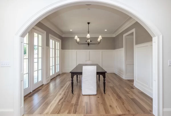 A dining room with a white archway and hardwood floors.