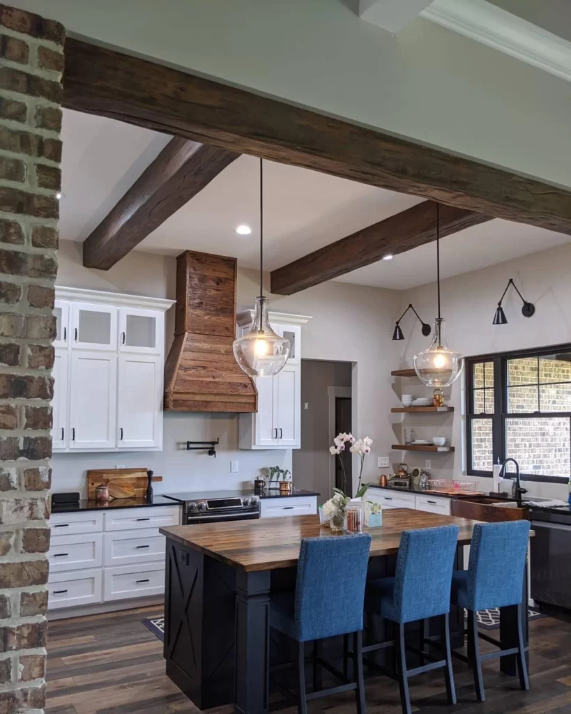 installed box beams in a modern kitchen with a wood range hood and a wood table with three blue chairs
