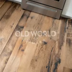 Close-up of reclaimed engineered mixed oak planks with blackened saw marks, patina, and wide grain character near kitchen stove.