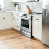 Sustainably sourced Modern Harvest Engineered Oak Flooring in a sunlit kitchen with white cabinetry and stainless steel appliances.