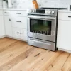 Close-up of Modern Harvest engineered oak flooring beneath a Frigidaire stove with white cabinets and brushed metal hardware.