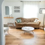 Wide living room shot with a warm brown couch and Modern Harvest engineered flooring, featuring eco-friendly oak planks with soft character marks.
