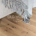 Detailed image of reclaimed white oak flooring beneath a textured gray throw, showing the natural beauty and imperfections of antique hardwood.