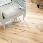 Wide shot of light-toned white oak engineered flooring with reclaimed characteristics, featuring subtle cracks and grain under a modern chair and coffee table.