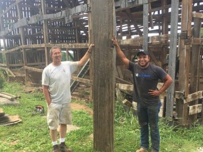 Two men standing in front of a barn after dismantling the timbers and boards that will be repurposed