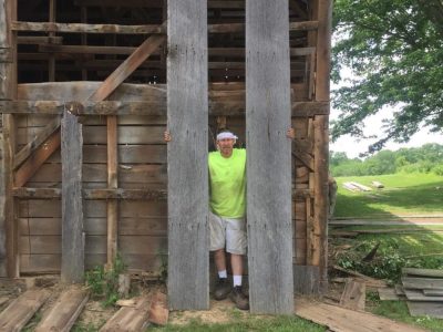 One of our guys standing in front of a barn after dismantling the timbers and boards that will be repurposed
