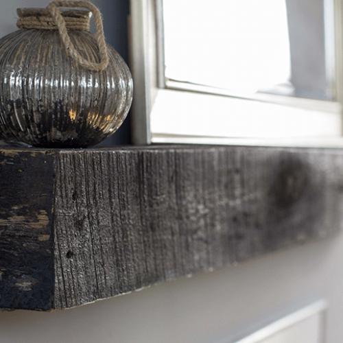 A reclaimed wood fireplace mantel with a mirror and a candle holder